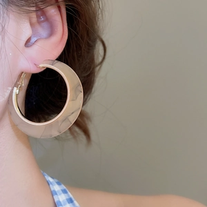 Close-up of a beige marble patterned acetate C-shaped hoop earring on a model's ear