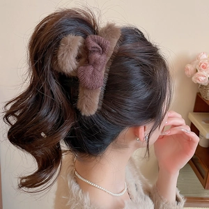Detail of plush faux fur shark clip with brown knitted bow on woman's ponytail