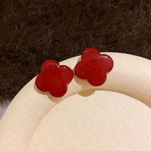 Macro view of red clover stud earrings with a glossy finish on beige textured stand