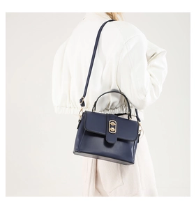 Side view of a navy blue flap crossbody bag with golden rings worn by a model in white