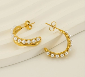 Détail de boucles d'oreilles dorées en C avec perles sur un support ondulé
