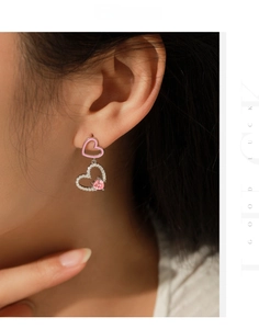 Dettaglio degli orecchini a cuore con smalto rosa e cristalli scintillanti indosso