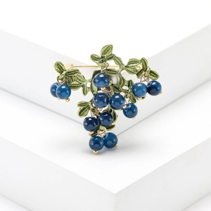 Detail of elegant gold cranberry brooch with green enamel leaves and blue fruit beads