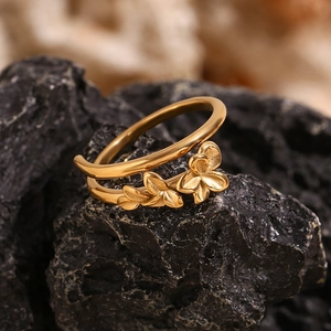 Macro detail of 18K gold-plated double-layer ring with delicate floral charms on rock