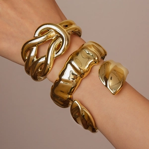 Close-up of three chunky gold bracelets with woven, wavy, and irregular metal textures