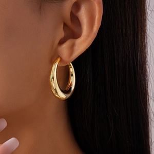 Close-up of a chunky polished gold round hoop earring worn on a female model's ear