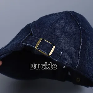 Detail of the bronze metal adjustable buckle on dark blue denim flat cap with twill texture
