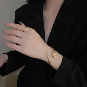 Detail view of the golden snake-shaped open bracelet and ring set with metallic luster