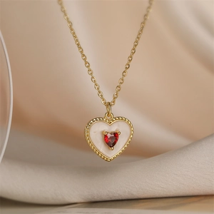 Close-up of gold hollow heart pendant with a red gemstone on a soft fabric background