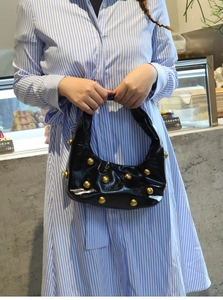 Detail of a black leather crescent shoulder bag with large gold spherical studs