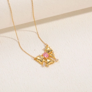 Detail of golden butterfly necklace with pink gemstone and zircon pavé on stone surface