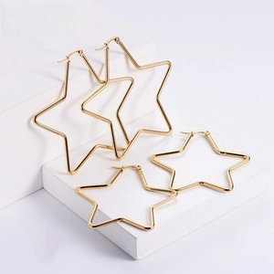 Detail of two sizes of gold-plated star-shaped hoop earrings on white geometric stands