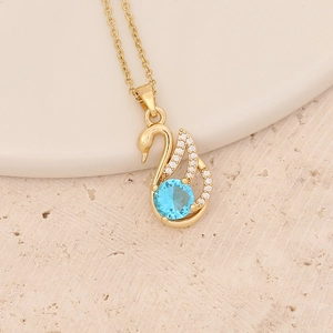 Detailed view of a golden swan pendant with a blue center stone on stone background