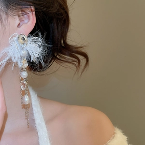 Close-up of elegant long tassel earrings with white feathers, pearls and crystals