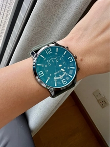 Close-up of the blue-green dial and silver case on a male wrist with green strap