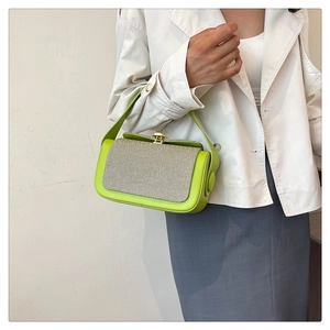 Detailed view of the green and beige contrast shoulder bag held by a model in a white coat