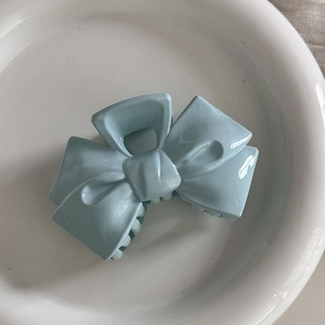 Macro shot of light blue bow-shaped hair claw clip on a white decorative ceramic plate