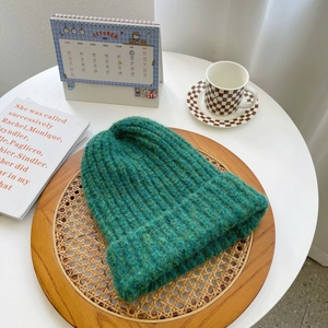 Macro view of forest green chunky knit beanie with ribbed texture on wooden tray