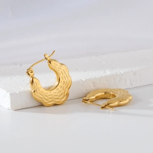 Detail of gold chunky hoop earrings with a unique wavy textured finish on a white base