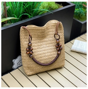 Detail of beige straw bag with dark wooden beads and brown handles on a wooden stool