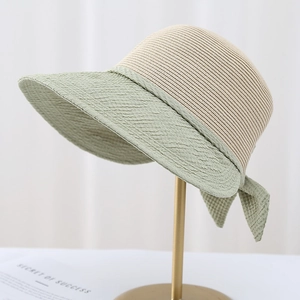 Women's chic wide brim straw sun hat with green ribbon bow on a minimal gold stand