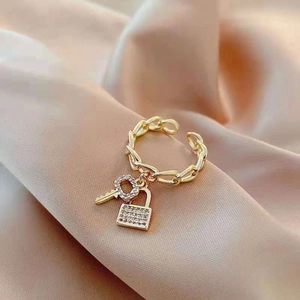 Détail d'une bague chaîne dorée avec breloque clé et cadenas sertie de cristaux
