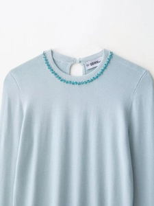 Detail of light blue knit top featuring exquisite floral rhinestone neckline decoration