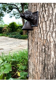 Close-up of rustic cast iron dog head door bell mounted on a tree in a garden setting