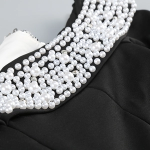 Detail of dark gown featuring intricate white pearls and shimmering rhinestone embellishments