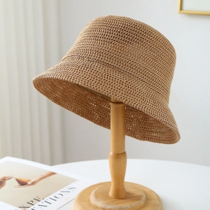 Cappello a secchiello in paglia intrecciata kaki su supporto in legno con luce naturale