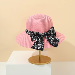 Dettaglio cappello di paglia rosa con fiocco a fiori neri su un supporto dorato
