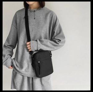 Close-up of a minimalist black nylon crossbody bag with a knotted zipper pull on the model