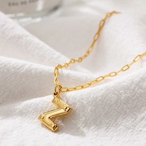 Detail of a gold letter N pendant with a textured finish on a stylish paperclip chain