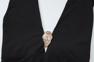 Close-up of deep V-neckline with golden metal oyster ornament on a black sleeveless dress