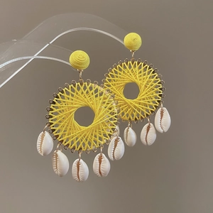 Detail of yellow woven hoop earrings featuring white shell pendants and gold metal accents