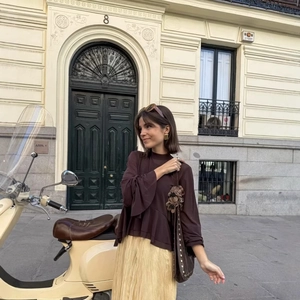 Elegant woman in brown ruffle top and pale yellow pleated maxi skirt standing outdoors