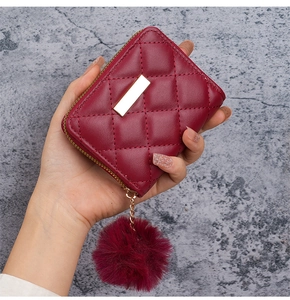 Dettaglio mini portafoglio rosso trapuntato con finiture oro e ciondolo a pompon
