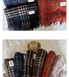 Close-up of multicolored plaid scarves with fringe edges and brand labels on a bed