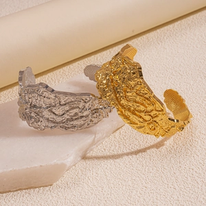 Irregular textured gold and silver metal cuff bracelets on white marble stone