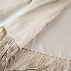 Dettaglio del cappotto di lana beige con nappe decorative a frange e fodera interna liscia