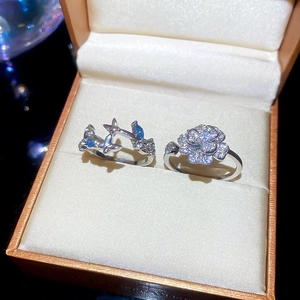 Detail of silver rings featuring zircon flower cluster and blue gemstone bird motifs