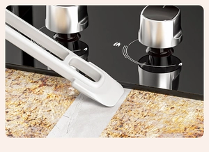 Close-up of a white kitchen crevice scraper removing grime from a stone surface