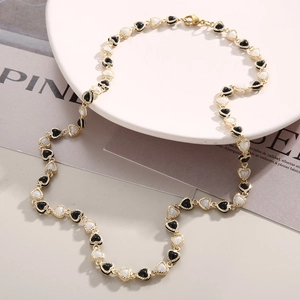 Elegant gold necklace featuring alternating black and white heart charms with beaded edges