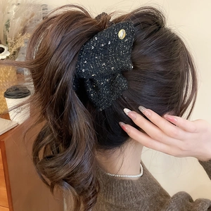 Detail of black tweed bow hair claw with gold metallic thread and engraved metal logo