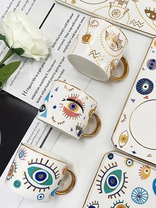 Macro detail of Evil Eye ceramic coffee cup with gold handle and matching saucer set