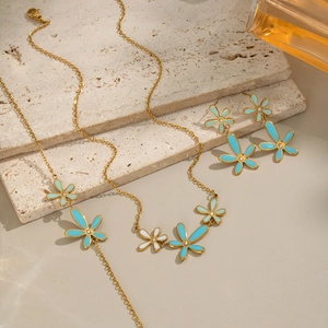 Detailed close-up of 18K gold-plated necklace and earrings with blue enamel flowers