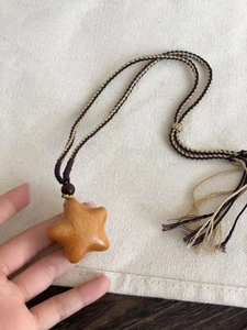 Hand holding a carved wooden star pendant with a handmade braided rope necklace cord