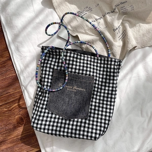 Detail of plaid canvas tote bag with denim pocket and colorful braided handles