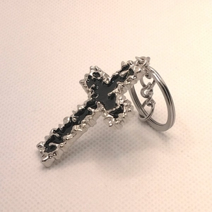 Close-up of silver metal cross keychain with black inlay and serrated edge texture
