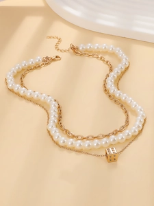 Detail of layered gold chain with pearl strand and cube dice pendant on a beige surface